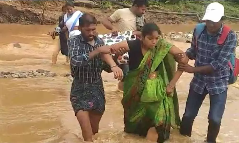 108 ambulance staff, Anganwadi worker and E Yugandar helping the pregnant woman in crossing the stream at Rollagadda village on Friday