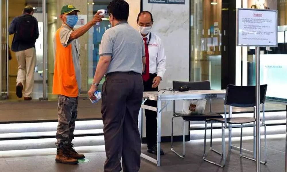 A man wearing a face mask uses a thermal scanner to check on the temperature of an individual before he can enter a building in Singapore (Photo | AP)