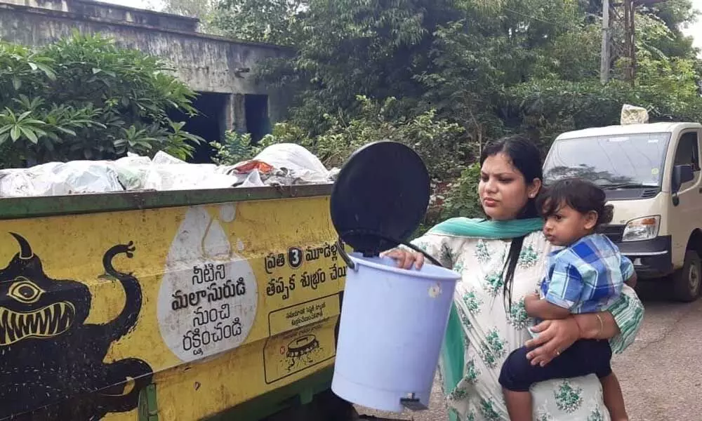 Municipal Commissioner Pamela Satpathy, with her child in one hand, emptying trash bin in a Swachh auto in Warangal on Monday
