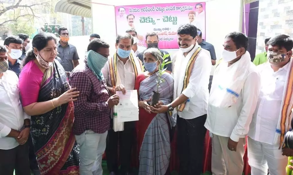 Chief Whip D Vinay Bhaskar giving away CMRF cheque to a poor woman while MP J Santosh Kumar giving a sapling at a programme at Balasamudram in Warangal on Thursday