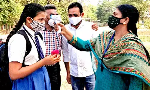 Students conducting the morning prayer inside the classroom. (Above) A teacher checking the temperature of a student before allowing her into the classroom on the first day of reopening of schools, in Warangal on Monday.