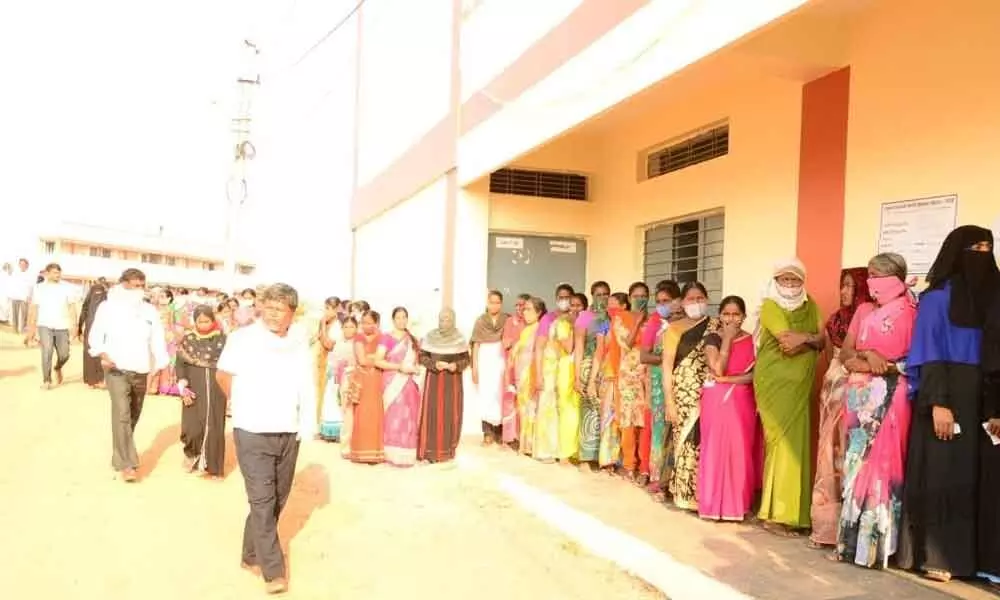 Voters stand in queue line to cast their votes at a polling station in Bhramanakotkur village on Wednesday