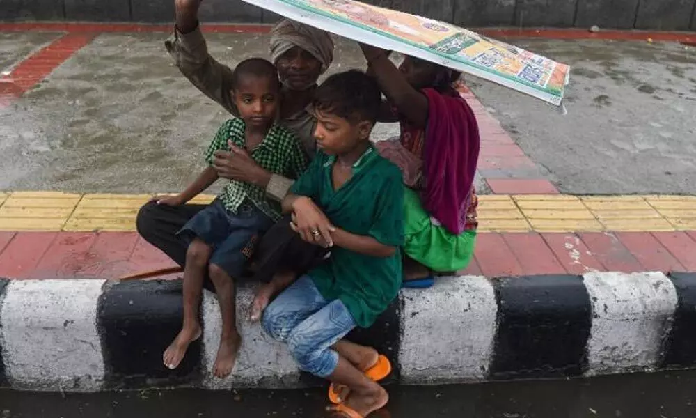 A family covers themselves under a hoarding during rain as monsoon reaches New Delhi. (Photo | PTI)