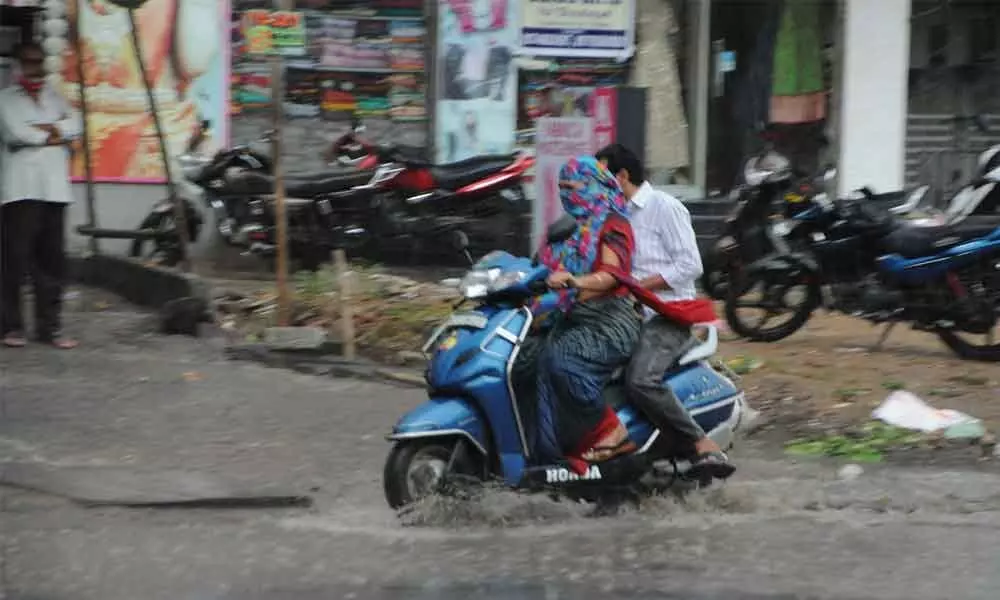 Two persons ride through a water-logged road in Guntur as the city experiences continuous drizzle on Thursday