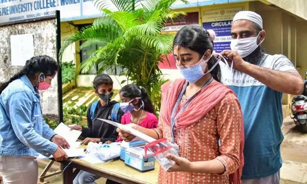 A volunteer helps a student to wear a face mask before she appears for the Common Entrance Examination (CET), at a college in Bengaluru, Saturday. Credit: PTI Photo  Read more at: https://www.deccanherald.com/state/top-karnataka-stories/karnataka-reports-1262-new-covid-19-cases-17-deaths-1024869.html