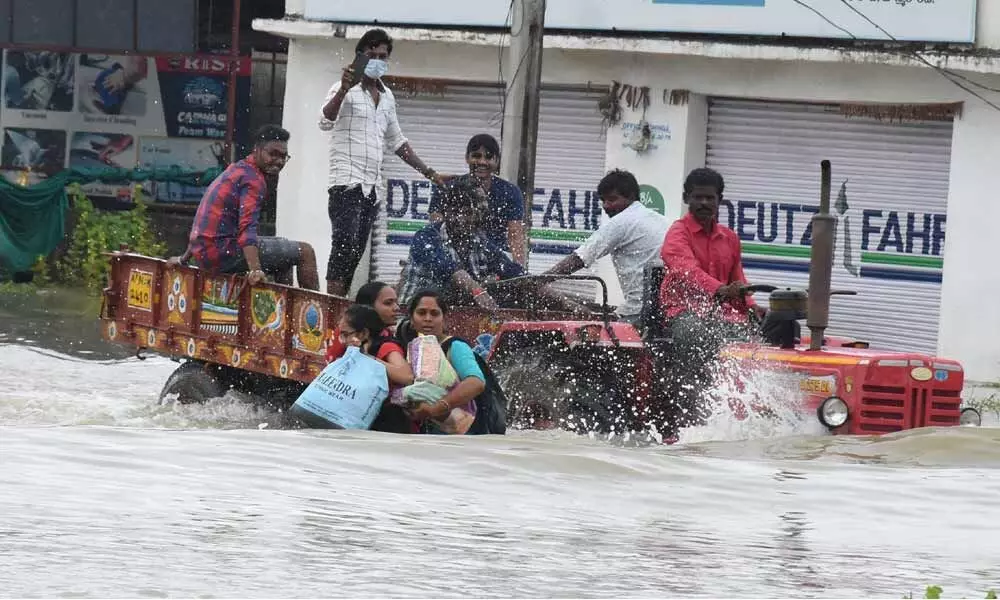 Women with essentials flee from their flooded homes to safer location, in Warangal on Tuesday Photo: G Shyam Kumar