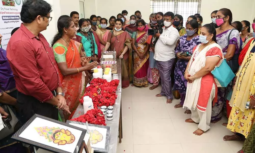 An instructor explaining the making of dry flower technology based products to women trainees