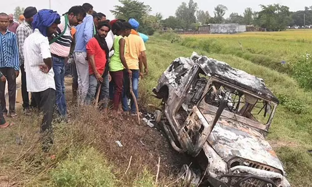 Villagers watch a burnt car which ran over and killed farmers on Sunday, at Tikonia village in Lakhimpur Kheri, Uttar Pradesh. (Photo | AP)