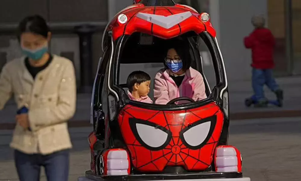A woman wearing a face mask to help protect from the coronavirus rides on a toy car with a child at a shopping mall in Beijing, Sunday, Oct. 24, 2021. (Photo | AP)