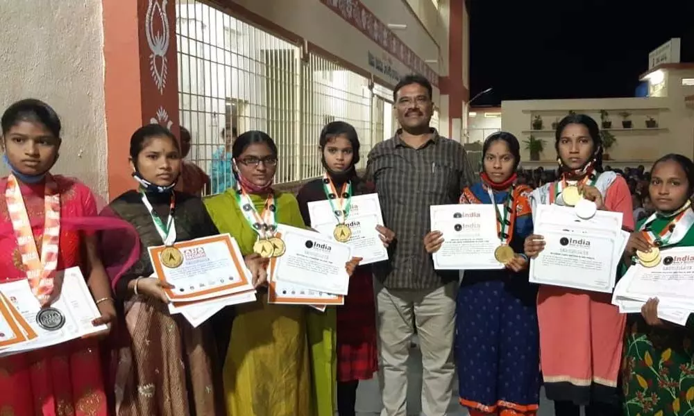 District Tribal Welfare Officer Mahaboob Basha felicitating the students with certificates, gold and silver medals in Alur. Principal of the school, Saraswathi is also seen.
