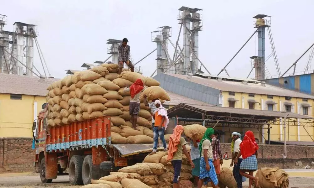 File photo of workers unloading paddy from a lorry in a parboiled rice mill in Miryalguda