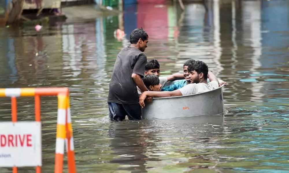 Young men sit in a vessel as another man pushes them on a waterlogged street following heavy rain in Chennai on Saturday