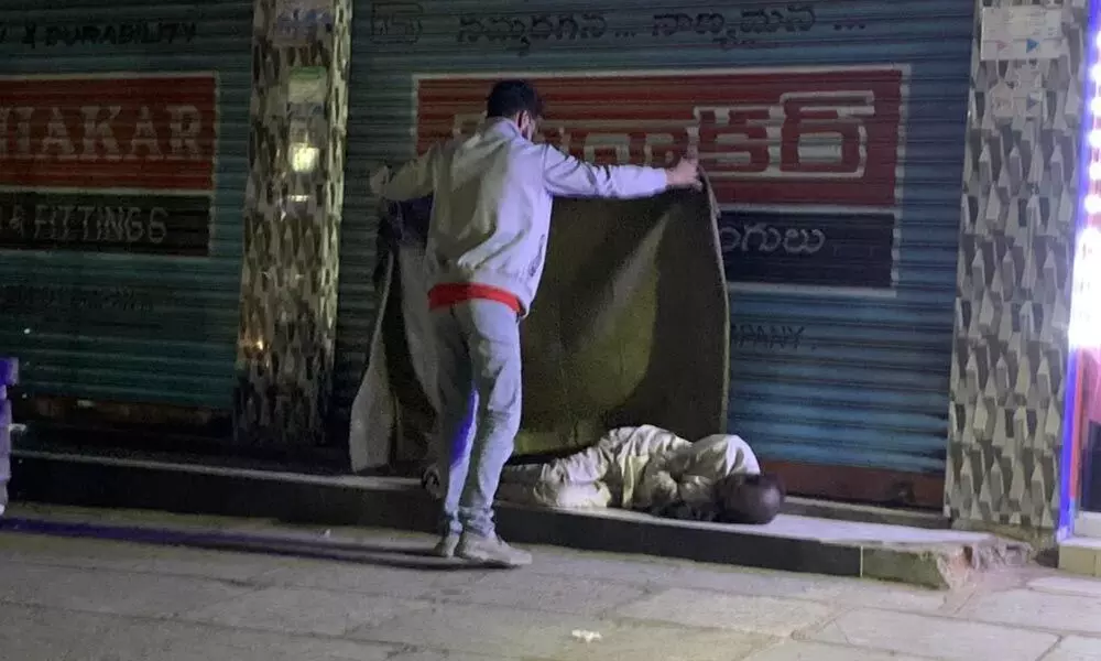 NGO member giving a blanket  to a man sleeping on footpath  in Hyderabad