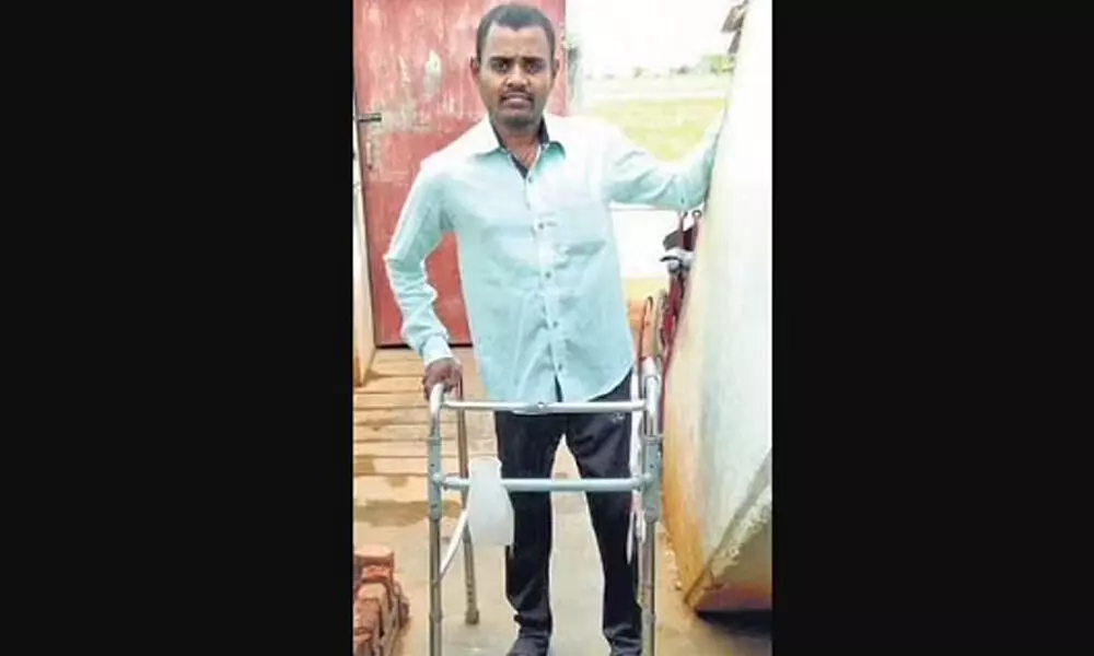 Adaikkalam Anandhan standing up for a moment using an assistive device, for a photo.