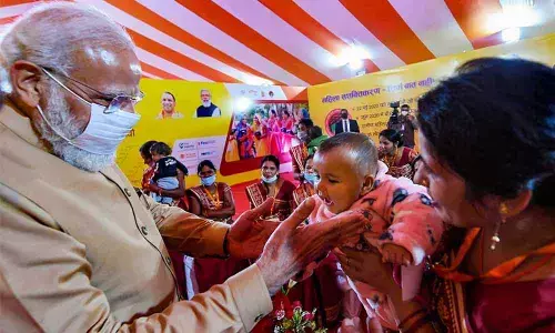 Prime Minister Narendra Modi interacts with a child of a woman during his interaction with women of self-help groups, in Prayagraj on Tuesday