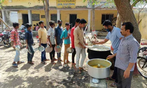 Students being served food under the trees due to lack of space in the kitchen shed at the Bodhan school