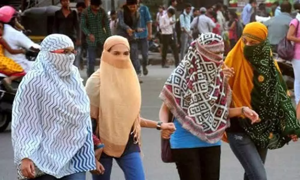 With mercury soaring, girls cover their faces with scarves while returning home from college on Ramnagar road in Anantapur