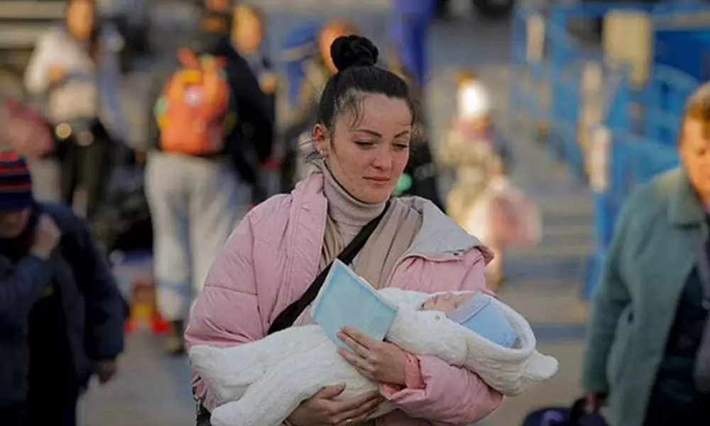 A refugee fleeing the war from neighbouring Ukraine walks with a baby in her arms after crossing the border by ferry at the Isaccea-Orlivka border crossing in Romania. (Photo | AP)