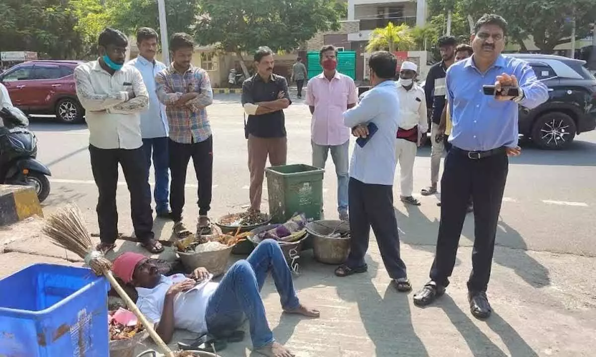 Corporator Murthy Yadav protesting by lying down on the road amid garbage filled buckets in Visakhapatnam on Wednesday.