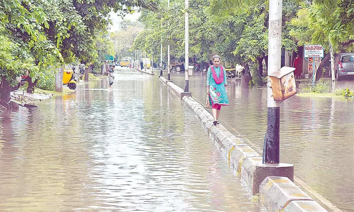 A girl walks on the divider of a flooded street at Devi Chowk in Rajamahendravaram on Friday