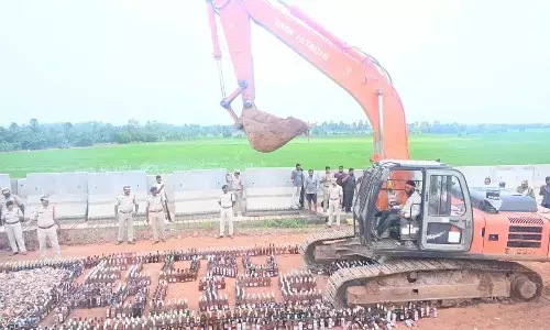 Police destroying liquor bottles seized in various cases, near ASRAM hospital in Eluru on Wednesday