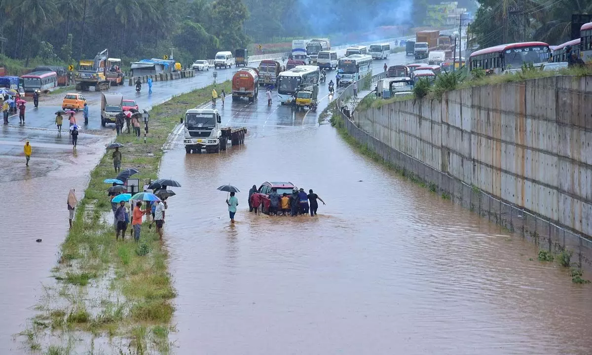 People push a car stuck on the flooded Bengaluru-Mysuru highway following heavy monsoon downpour at Ramanagara  on Monday