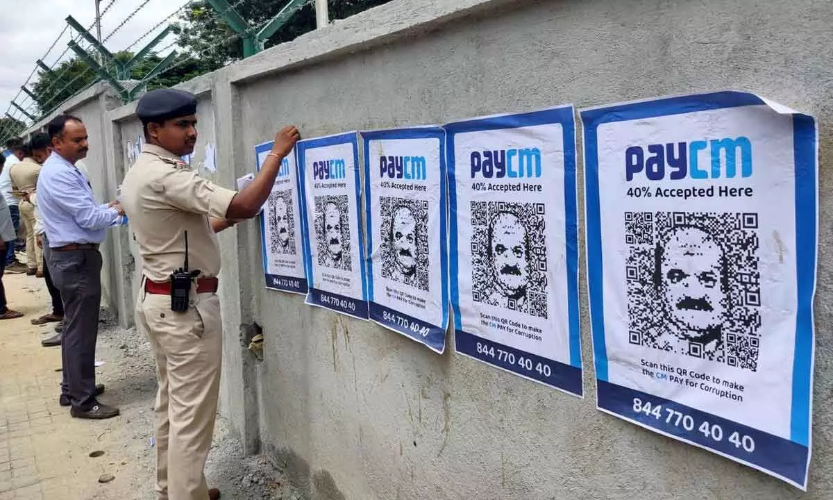 A police person removes posters with QR code and the phrase ‘PayCM’ written above targetting Karnataka Chief Minister Basavaraj Bommai, in Bengaluru