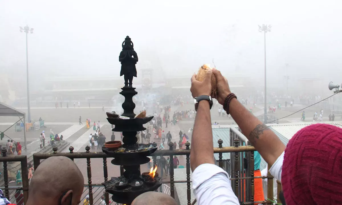 A devotee praying with folded hands after breaking coconut at Akilandam, looking at direction of Tirumala shrine though his vision blurred due to thick fog in Tirumala on Sunday
