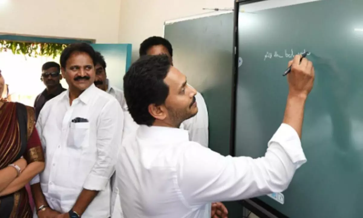 Chief Minister Y S Jagan Mohan Reddy writes on a digital board in classroom after distributing Jagananna Vidya Kanuka kits in Palnadu district on June 12