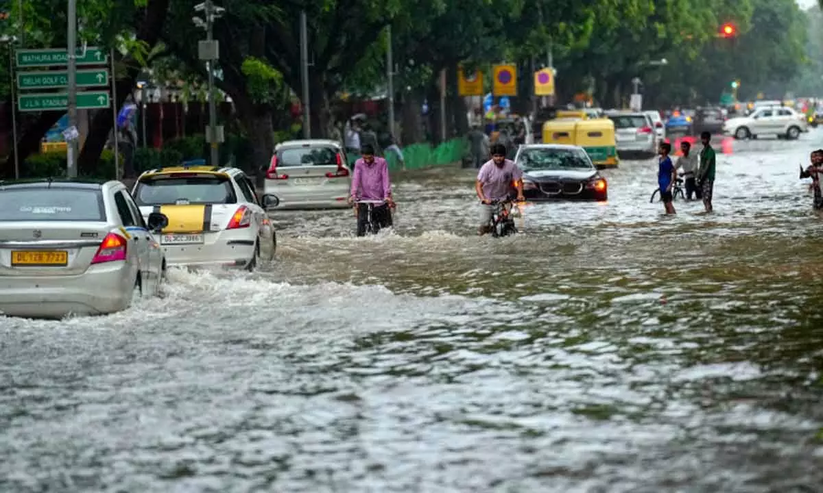 Commuters move through a waterlogged road at Rabindra Nagar after monsoon rain, in New Delhi on Sunday