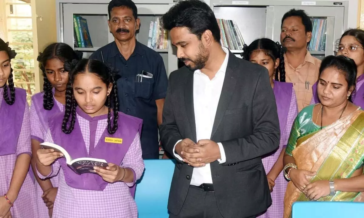 Collector Prasanna Venkatesh helping a student read a book at a newly-opened library in a school in Eluru on Monday