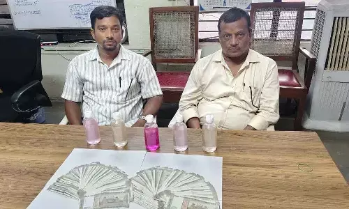Accused officials Anandeshi Raghavender and Medi Vinod seated with the seized cash bribe of Rs 1 lakh and chemical solution bottles used during the Anti-Corruption Bureau trap operation in Hyderabad on Monday