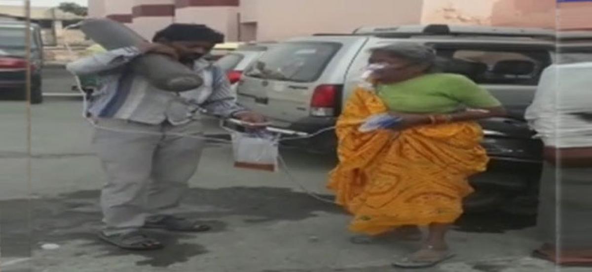 Man awaits ambulance while carrying mothers oxygen cylinders on shoulder